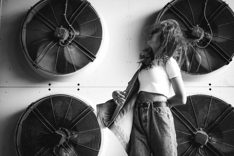 Young woman standing against electric fans mounted wall
