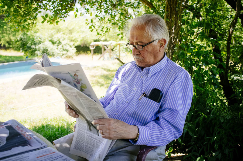 Senior man reading newspaper while sitting against tree