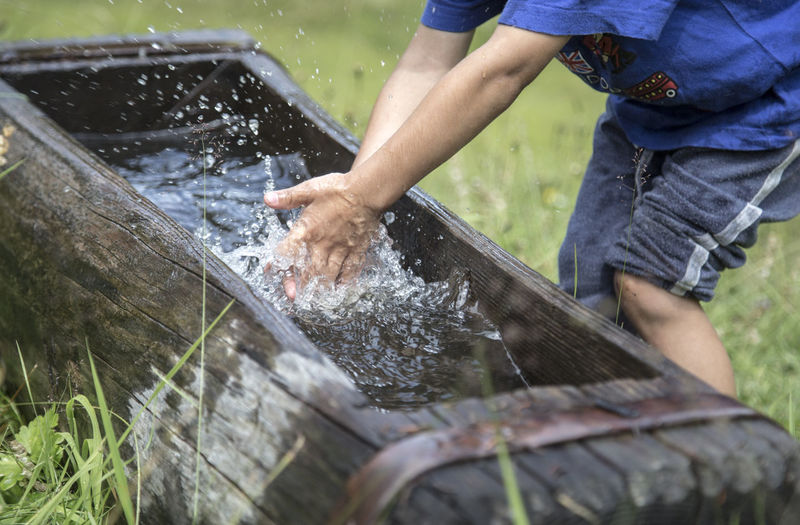 Midsection of boy washing hands in trough on field