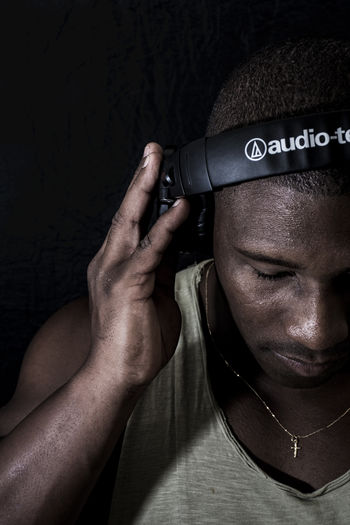 Close-up of young man listening music against black background