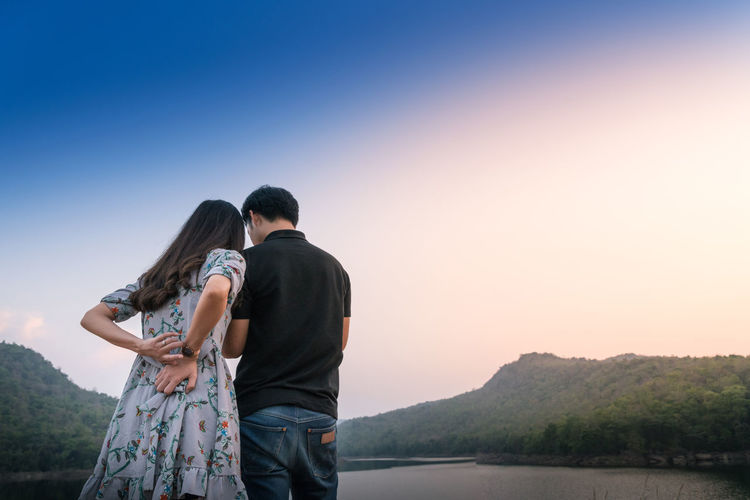 Rear view of couple standing on mountain against clear sky