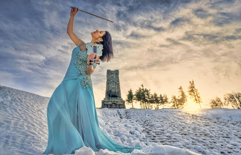 Woman playing on violin against sky during sunset