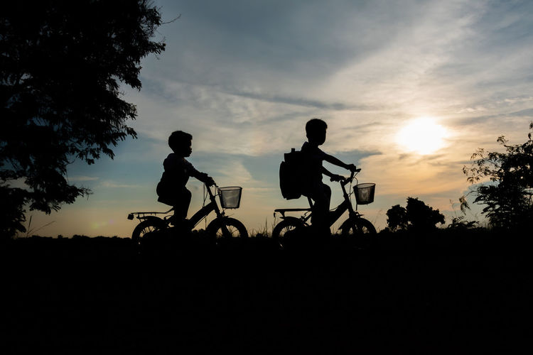 Silhouette people riding bicycles against sky during sunset