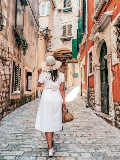 WOMAN WALKING ON STREET AMIDST BUILDINGS