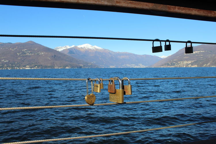 Padlocks hanging on railing by sea against clear sky
