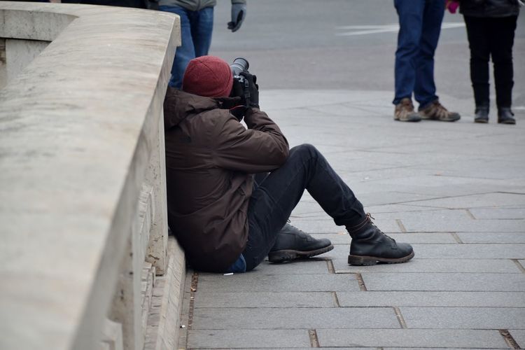 Side view of man photographing while sitting on street in city