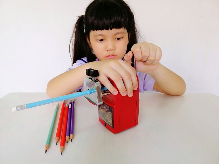 Cute girl sharpening pencil on table