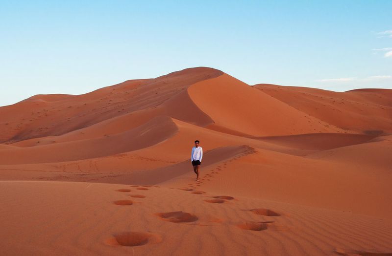 Man walking on sand dune at sahara desert against sky