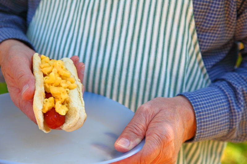 Man with macaroni and cheese hot dog outside