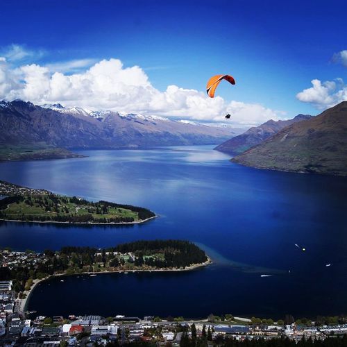 Low angle view of person paragliding over sea by city and mountains against sky