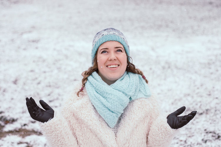 Smiling young woman standing at park during snowing