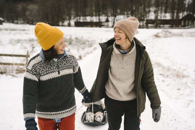 Smiling lesbian couple looking at each other while pulling daughter on snow