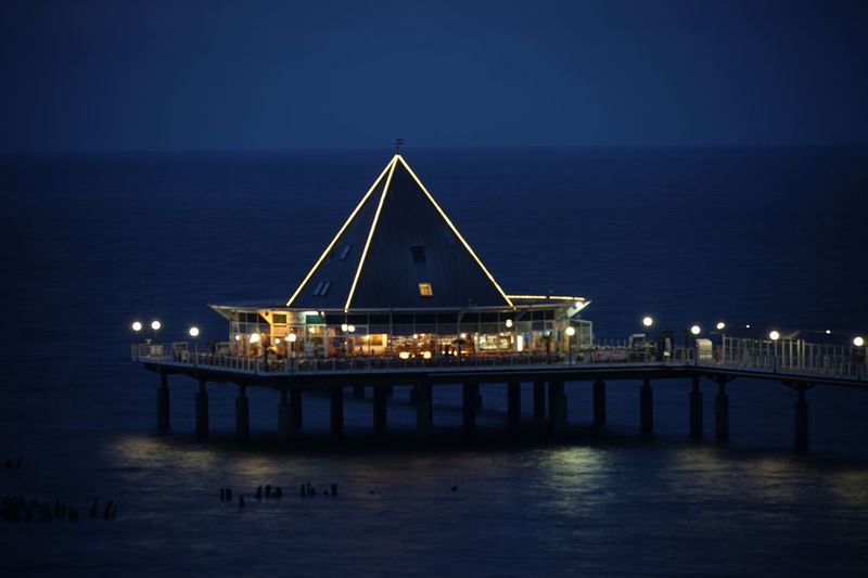 Illuminated restaurant on pier over sea against sky at night