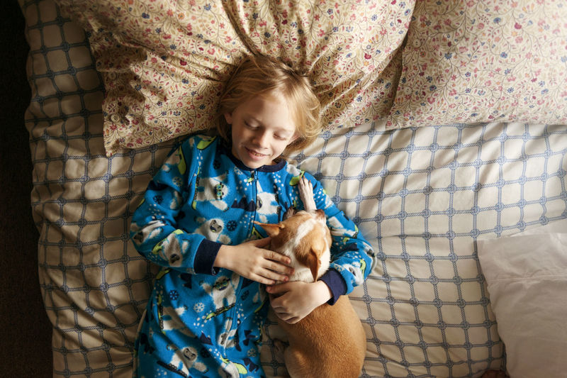 Overhead shot of smiling boy sleeping with dog on bed