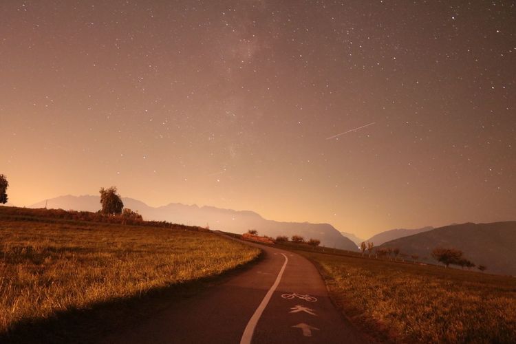 Road amidst field against sky at night