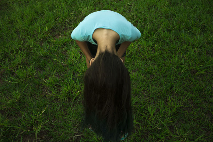 High angle view of girl with long hair bending on grassy field