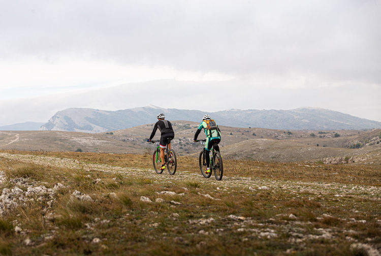 People riding bicycle on mountain against sky