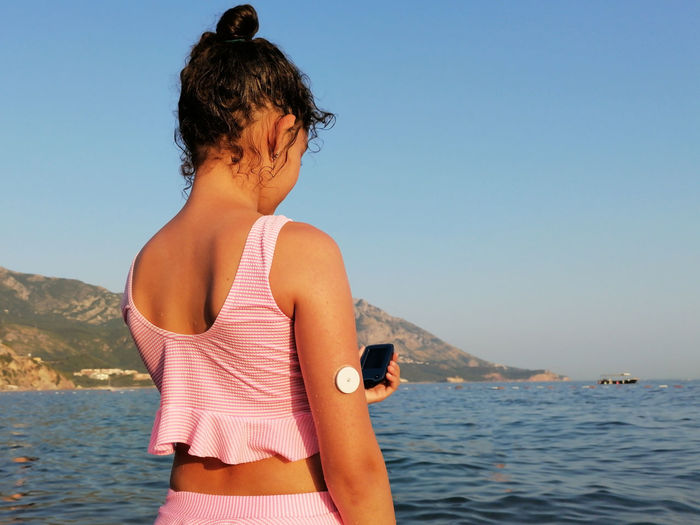 Girl with diabetes checks glucose level with cgm device before enters the sea.  medical equipment