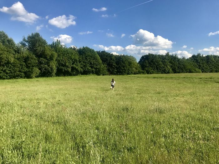 Young woman running on grassy field against sky