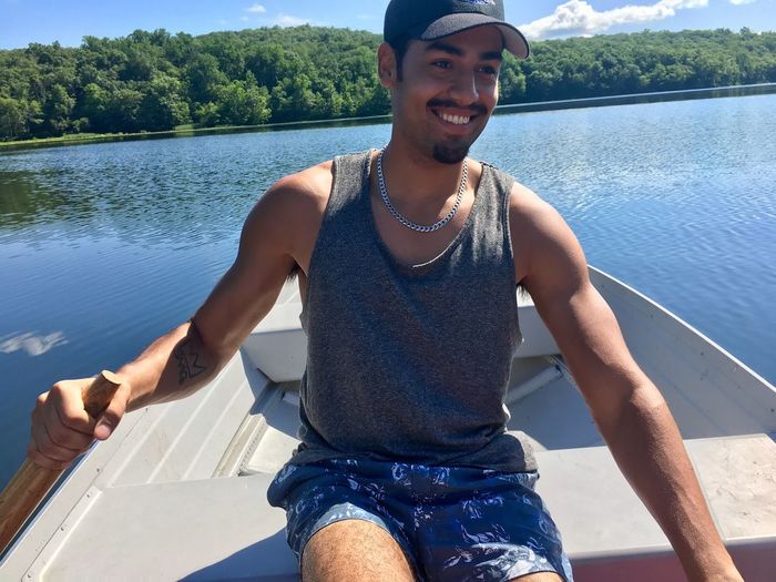Smiling young man traveling in boat on lake during sunny day