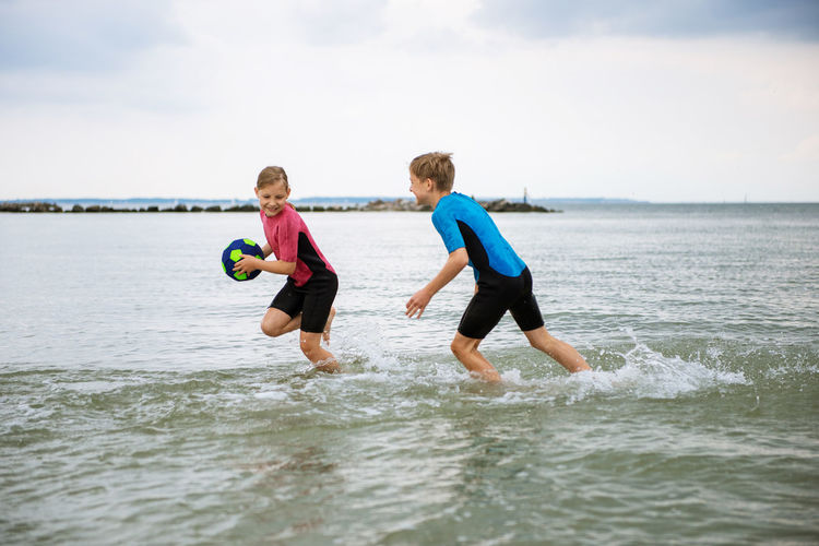 Playful friends playing with soccer ball in sea