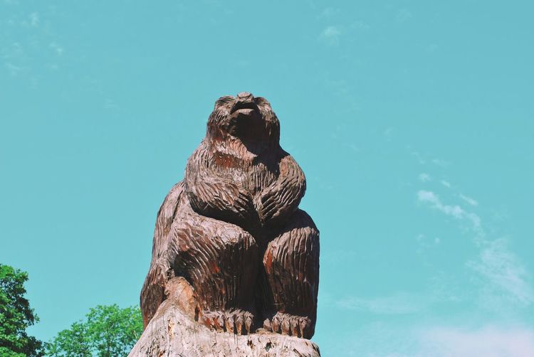 Low angle view of a wooden bear statue against blue sea
