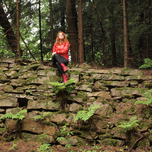 Low angle view of woman sitting on stone wall in forest during monsoon