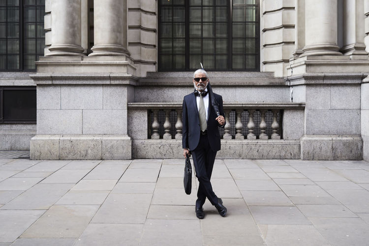 Uk, london, portrait of stylish businessman with sunglasses and umbrella wearing suit and tie