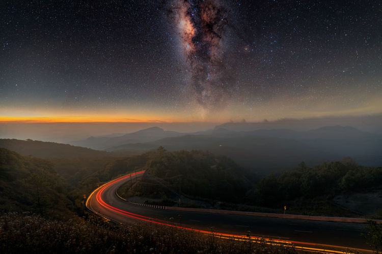 Light trails on road against starry sky at night