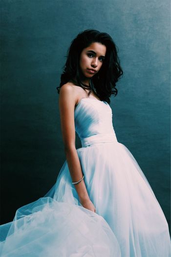 Portrait of young woman in white dress standing against wall