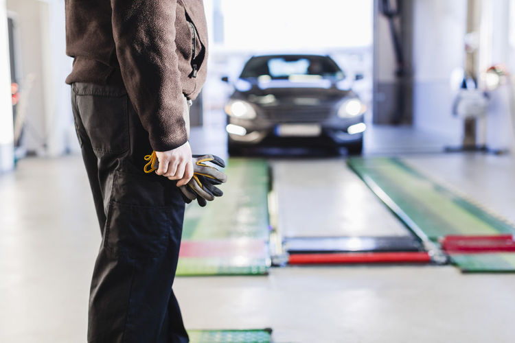 Midsection of mechanic standing in front of car coming towards hydraulic lift