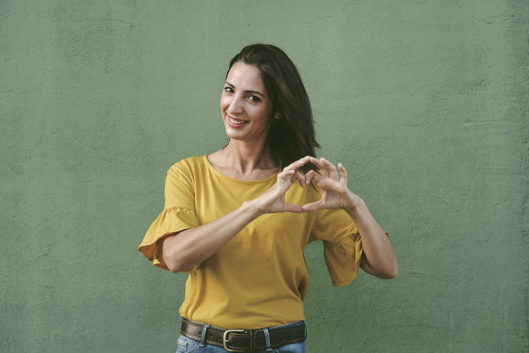 Portrait of smiling woman gesturing while standing against wall