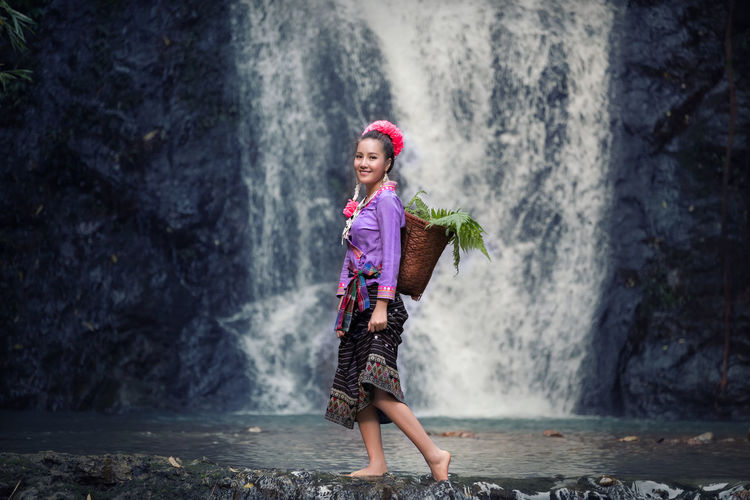 Full length portrait of young woman standing against waterfall