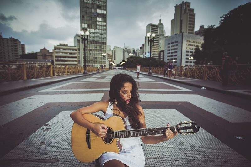 Young woman playing guitar while standing on road