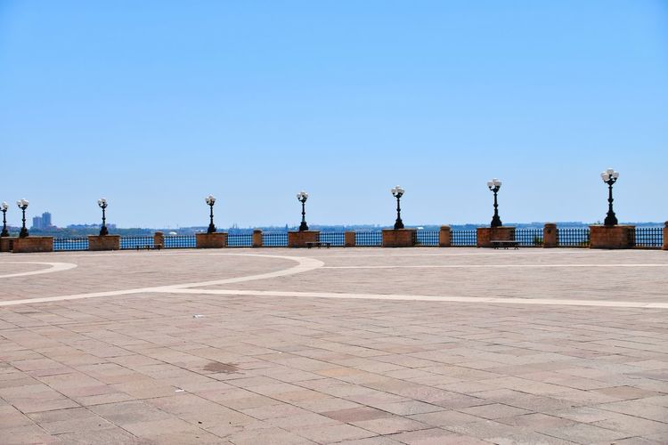 Empty footpath by street against clear blue sky