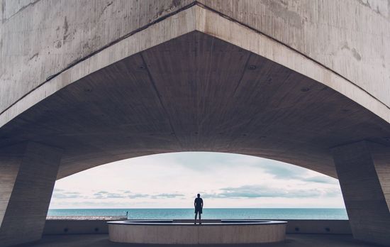 Rear view of man standing under bridge by sea
