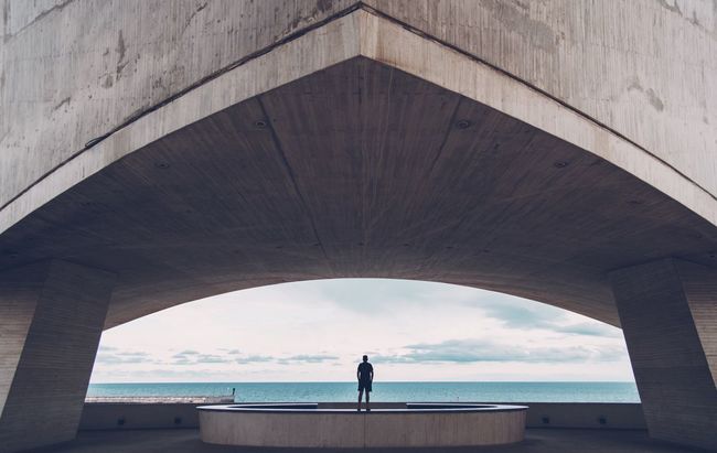 Rear view of man standing under bridge by sea
