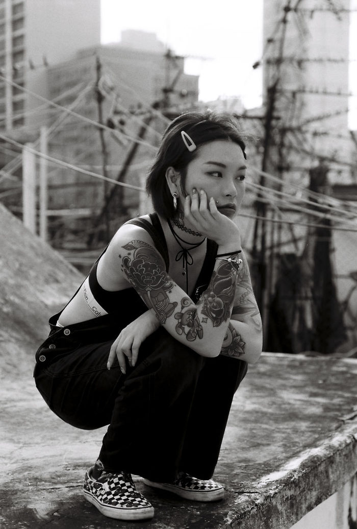 Thoughtful young woman with tattoos crouching on retaining wall at building terrace