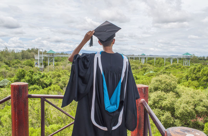 Rear view of man wearing graduation gown at observation point against forest