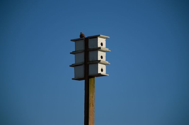 Low angle view of wooden post against clear blue sky