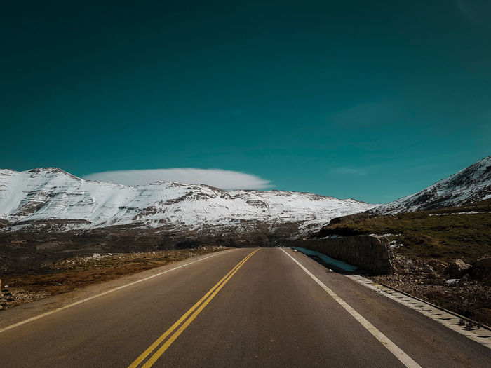 Road by mountains against sky during winter
