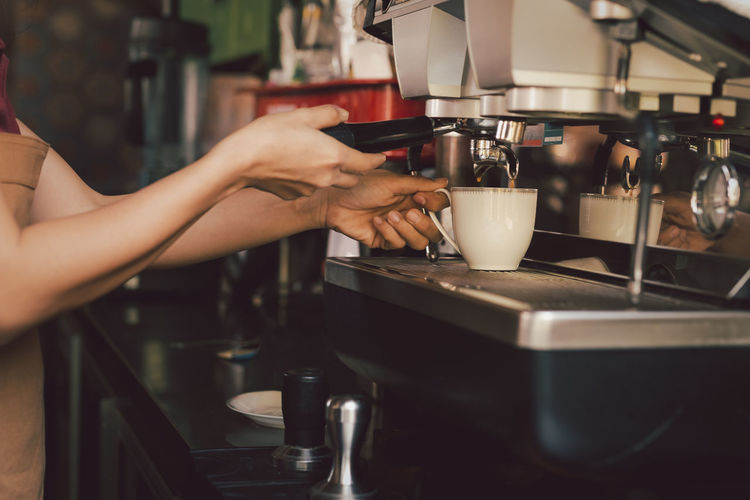 Female barista making cup of coffee with coffee machine in cafe.