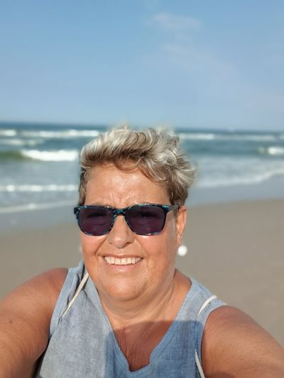 Portrait of woman wearing sunglasses on beach against sky