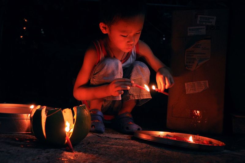 Boy igniting candles during festival at night
