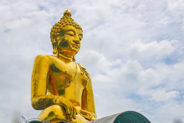 Low angle view of large golden buddha statue against sky