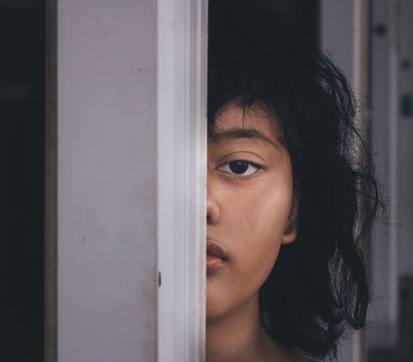 Close-up of young woman looking through window at home
