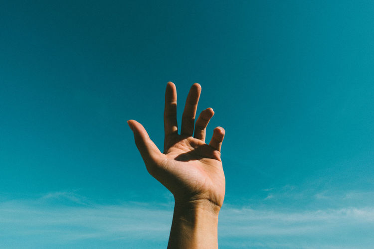 Cropped hand of woman against blue sky