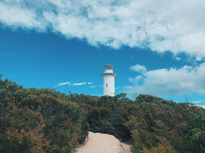 Lighthouse amidst trees and buildings against sky