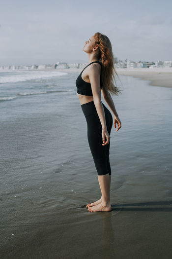 Young woman standing with eyes closed on shore at beach