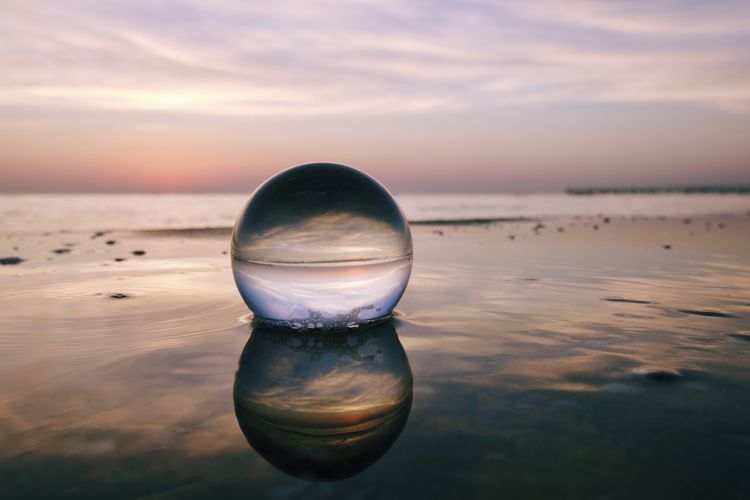 Close-up of crystal ball in water on beach against sky during sunset